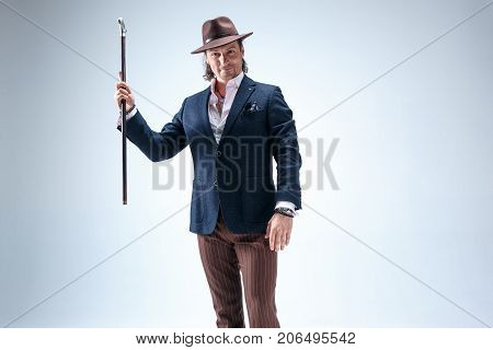 The mature man in a suit and hat holding cane. Isolated on a gray studio background.