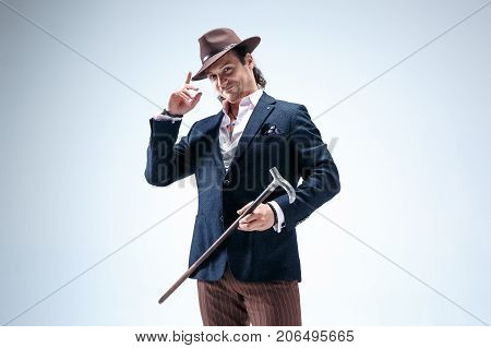 The mature man in a suit and hat holding cane. Isolated on a gray studio background.