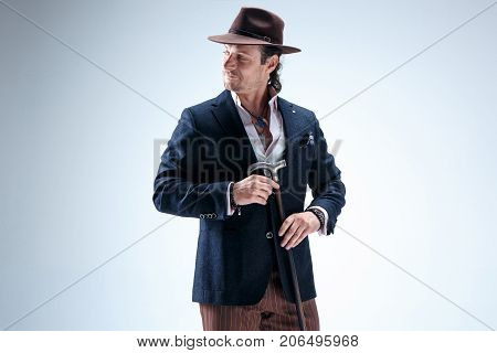 The mature man in a suit and hat holding cane. Isolated on a gray studio background.