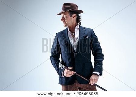 The mature man in a suit and hat holding cane. Isolated on a gray studio background.