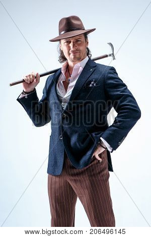 The mature man in a suit and hat holding cane. Isolated on a gray studio background.