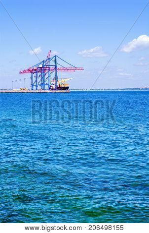 Container ship in the port on the horizon. Port crane loads a container on a ship. Cargo transportation by sea.