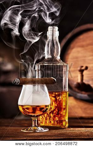 Glass of cognac or brandy with smoking cigar on wooden table.Glass ful of smoke