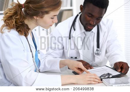Happy smiling african american male doctor talking with colleague while sitting at the table.