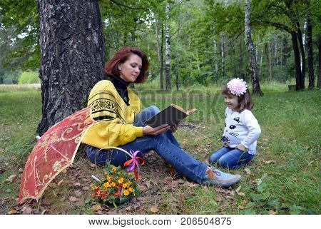 family mom and daughter reading a book in the woods