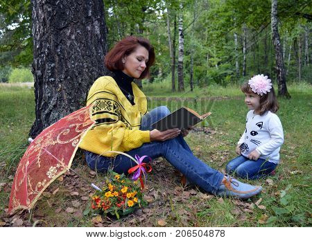 family mom and daughter reading a book in the woods