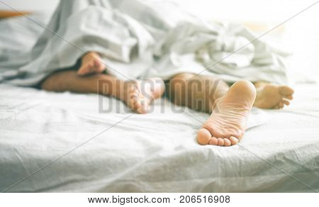 Close up of male and female feet on a bed - Loving couple having sex under under white blanket in the bedroom - Concept of sensual and intimate moment of lovers - Vintage filter - Focus on male foot