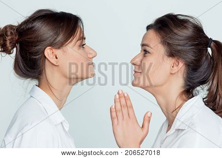 Studio profile portrait of young female twins sisters on gray