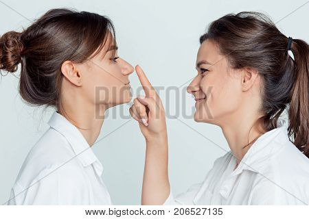 Studio profile portrait of young female twins sisters on gray