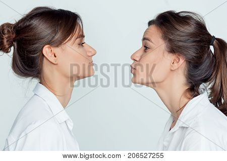 Studio profile portrait of young female twins sisters on gray