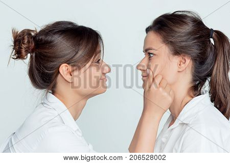 Studio profile portrait of young female twins sisters on gray