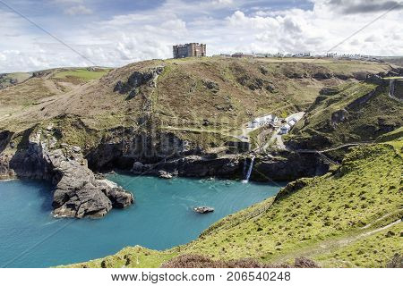 Tintagel, Cornwall, UK: April, 2016: A view of the main entrance to Tintagel Castle in the valley and Hotel Camelot on the cliff. There is a beach cafe, visitors centre at the entrance.