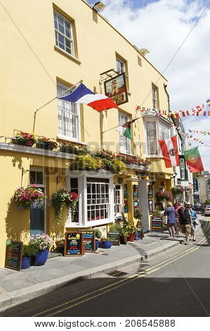 Tenby, UK: July 05, 2016: Tourists walk past the brightly painted Buccaneer Inn in Tenby. A very popular pub with visitors during the summer time with its flags and hanging baskets.