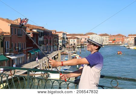 cute boy with glasses and hat makes a selfie with the smartphone on the bridge of the island of Murano near Venice in Italy