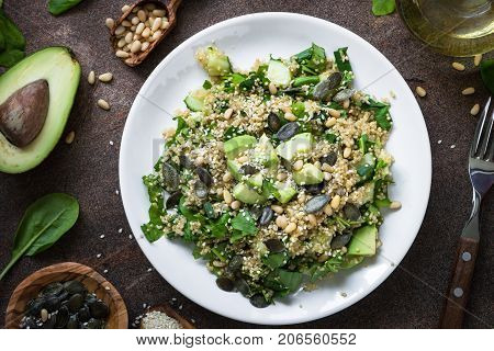 Vegan food. Fresh quinoa salad with spinach avocado greens seeds and Pine nuts in white plate on rusty stone table. Top view.