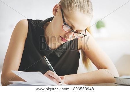 Portrait of young european woman doing paperwork at modern office desk with items. Secretary accounting project concept