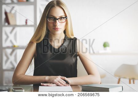Portrait of focused young woman doing paperwork at modern office desk with items. Secretary accounting project concept