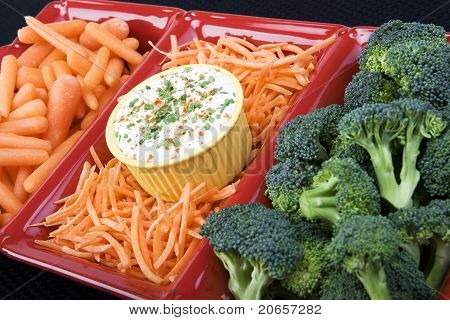 række rå gulerødder og broccoli i en rød keramisk fad med ranch dip