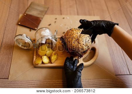 A top view of a fresh juicy meat burger and rustic potatoes on a wooden cutting desk. Fast food composition on a wooden table background, close-up. American burger. Cooking, fast food, concept.