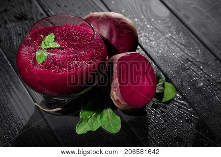 A close-up picture of bright red beet smoothie in a glass on a black table background. Juicy beetroots with fresh salad leaves and green decorative mint. Detoxification and dietary concept.