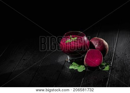 A spacious glass full of dark purple beetroot cocktail on a black table background. Nutritious beets for a healthful vegetarian salad. Vegetable juices for gourmets. Copy space.