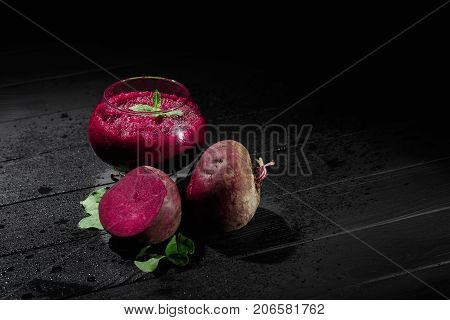 A spacious glass full of dark purple beetroot cocktail on a black table background. Nutritious beets for a healthful vegetarian salad. Vegetable juices for gourmets. Copy space.
