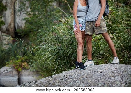 Sport legs. Woman and her man hiker climbing rock on mountain near the river. Assistance. Concept of sport and active life. Help, support, assistance in a dangerous situation