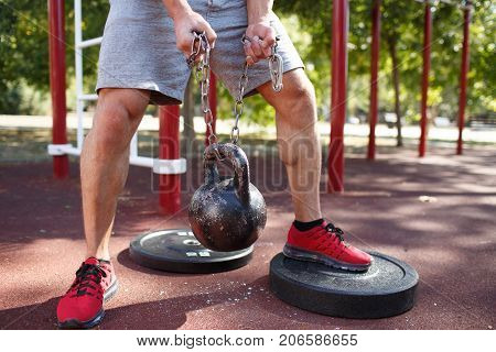 A strong man with sexy body is doing exercises on his feet. A handsome young man lifts weights with his feet in the park.