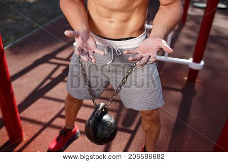 A strong man with sexy body is doing exercises on his feet. A handsome young man lifts weights with his feet in the park.