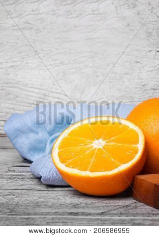 A gray wooden table with unpeeled vivid health-giving oranges full of vitamins, a wooden board and a blue napkin on a light gray wooden background.