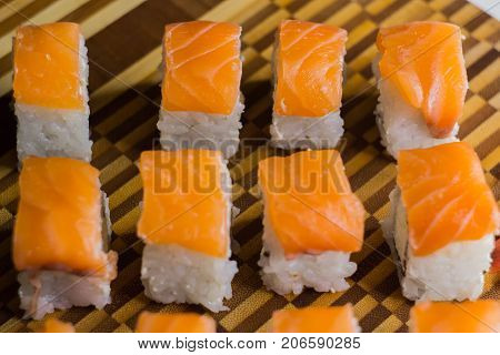 The set of salmon rolls on bamboo board. Focus on top line