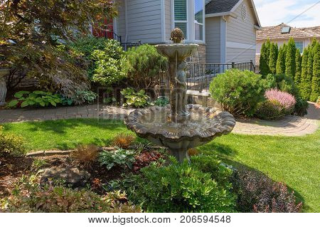 Water Fountain and brick garden path along manicuredhouse frontyard green grass lawn with plants trees and shrubs