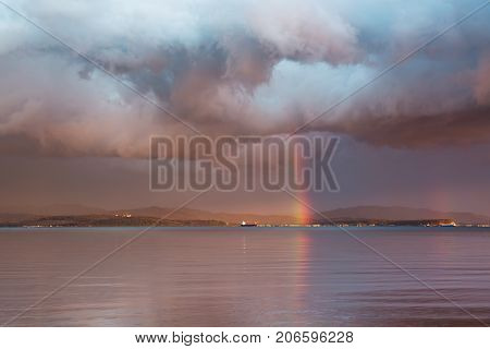 Landscape with dramatic sky rainy clouds and rainbow. Rainbow between the sky and sea surface.