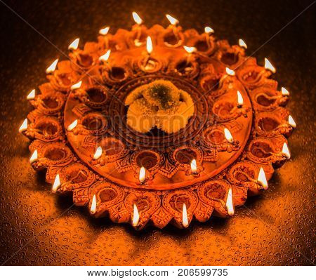Stock Photo of an illuminated terra-cotta Diwali lamp or Diya with detailed artwork on it. on a moody background and selective focus
