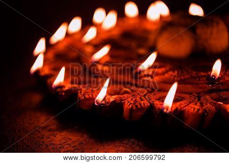 Stock Photo of an illuminated terra-cotta Diwali lamp or Diya with detailed artwork on it. on a moody background and selective focus