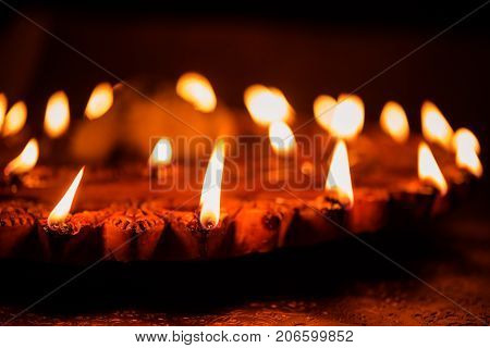 Stock Photo of an illuminated terra-cotta Diwali lamp or Diya with detailed artwork on it. on a moody background and selective focus