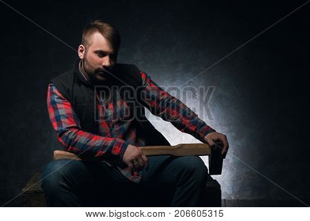 Dangerous-looking axeman. Lumberjack with weapon. Armed rural man with axe on dark background closeup, spooky atmosphere, danger concept