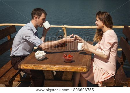happy young couple drinking tea outdoors, beautiful lovers man and woman have a good time on pier with a cup of tea