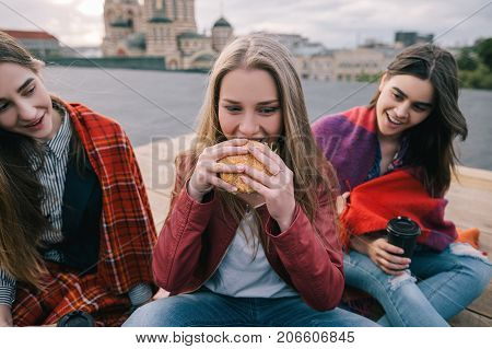 Young hot-eyed girl eats burger. Meeting friends with takeaway junk food. Overnutrition and diet failure, mood swing in eating. Close up picture