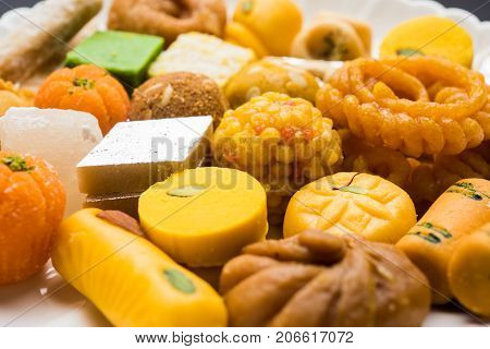 stock photo of Indian sweet or mithai and oil lamp or diya with gift box and flowers on decorative or colourful background, selective focus