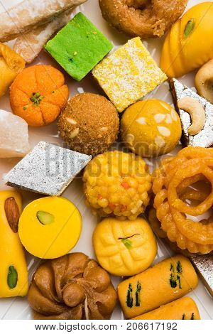 stock photo of Indian sweet or mithai and oil lamp or diya with gift box and flowers on decorative or colourful background, selective focus