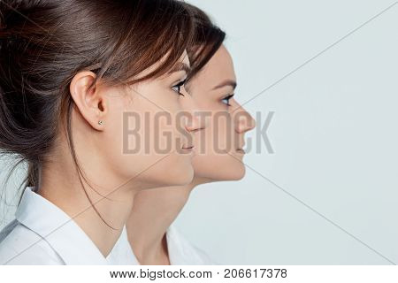 Studio profile portrait of young female twins sisters on gray