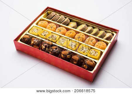 stock photo of Indian sweet or mithai and oil lamp or diya with gift box and flowers on decorative or colourful background, selective focus