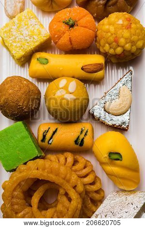 stock photo of Indian sweet or mithai and oil lamp or diya with gift box and flowers on decorative or colourful background, selective focus