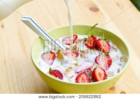 A bowl of cornflakes and strawberries, pour milk into a bowl