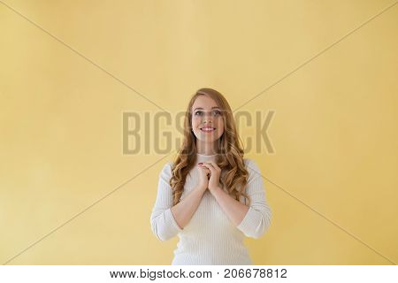 Superstitious hopeful young woman with wavy hair smiling cheerfully holding clasped hands in front of her while praying before exams or job interview. Positive cute woman expressing gratitude