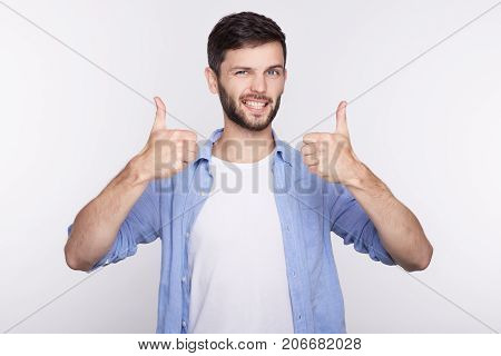 Portrait of a happy young successful male office worker giving two thumbs up gesture in full confidence isolated on studio wall background. Positive human emotion facial expression body language.