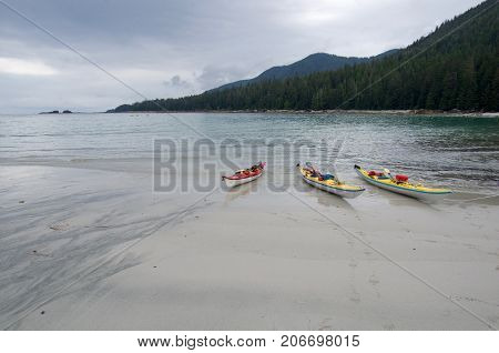 Three sea kayaks pulled up on a sandy beach on the Brookes peninsula Vancouver Island. Gray cloudy sky.
