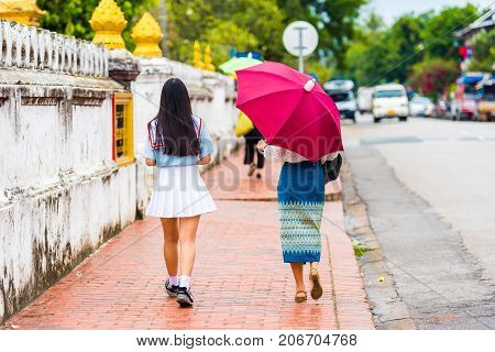 People On A City Street Under An Umbrella In Louangphabang, Laos. Copy Space For Text.