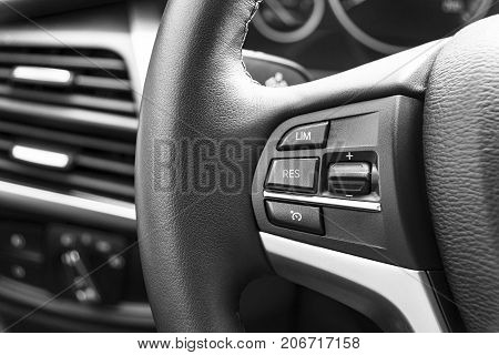 Cruise control buttons on the steering wheel of a modern car car interior details. Black and white
